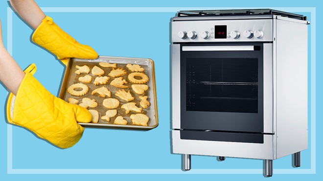 person holding a tray of cookies next to a freestanding oven